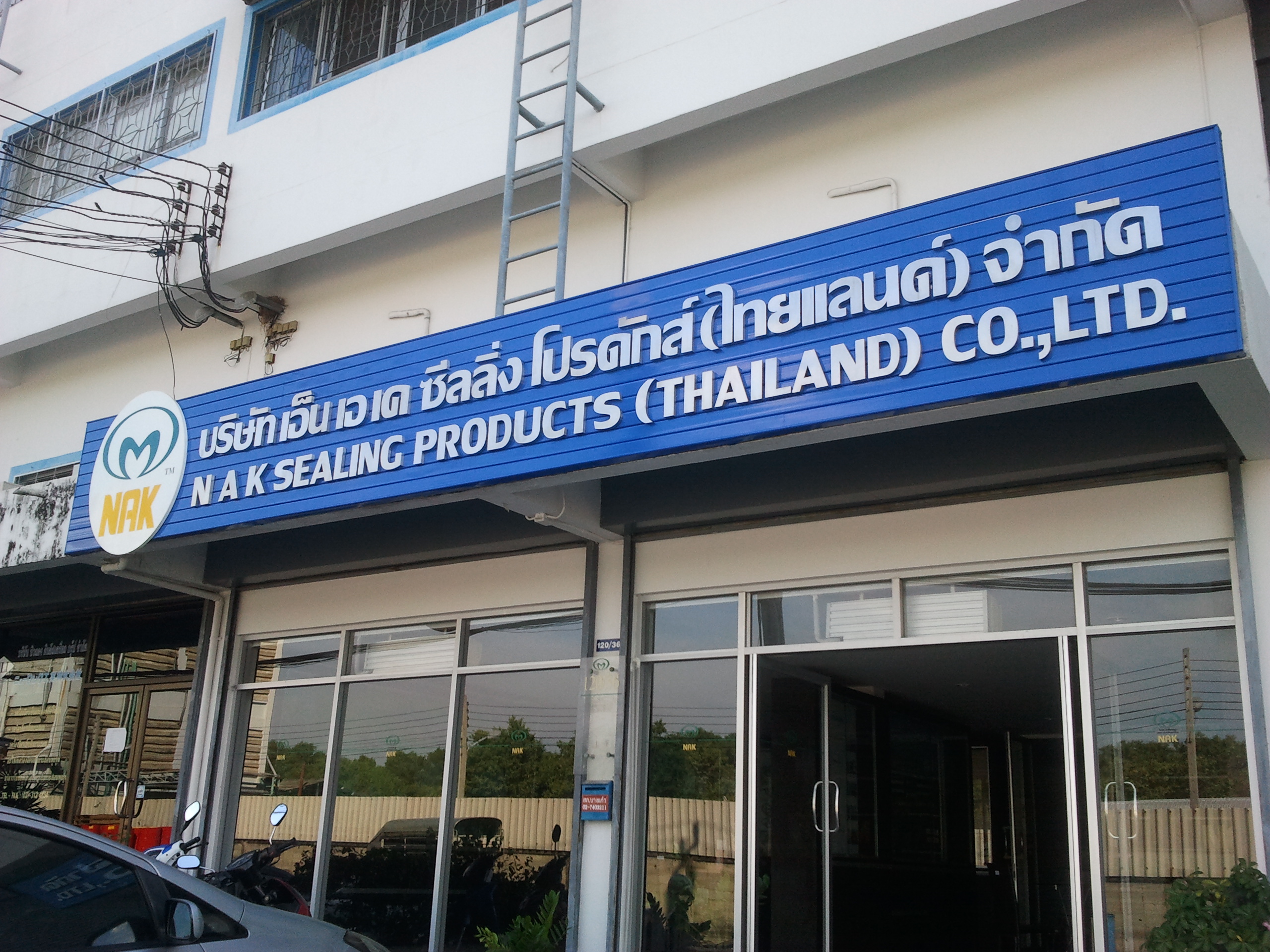 ป้ายหน้าอาคาร NAK Sealing Products Thailand สีน้ำเงินพร้อมโลโก้ M