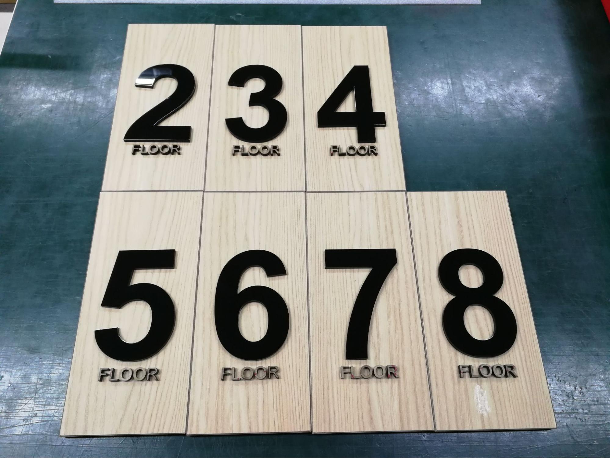 ป้ายบอกชั้นคอนโด ตัวเลขชั้น 2-8 พร้อมคำว่า FLOOR วัสดุอะคริลิกสีดำบนพื้นลายไม้สีอ่อน
