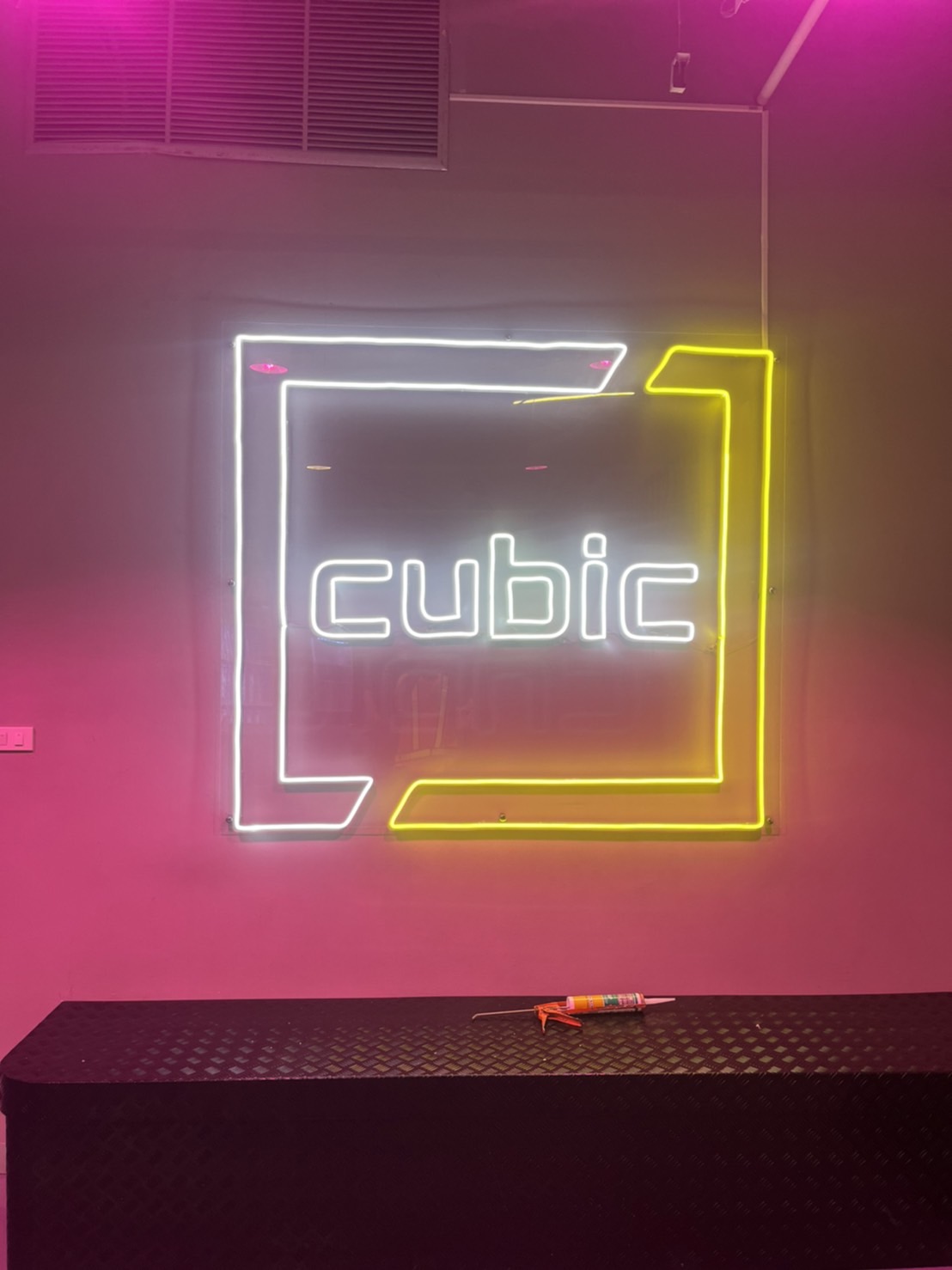 ป้ายนีออน cubic สีขาวในกรอบเรขาคณิตสีเหลืองบนผนังสีชมพู