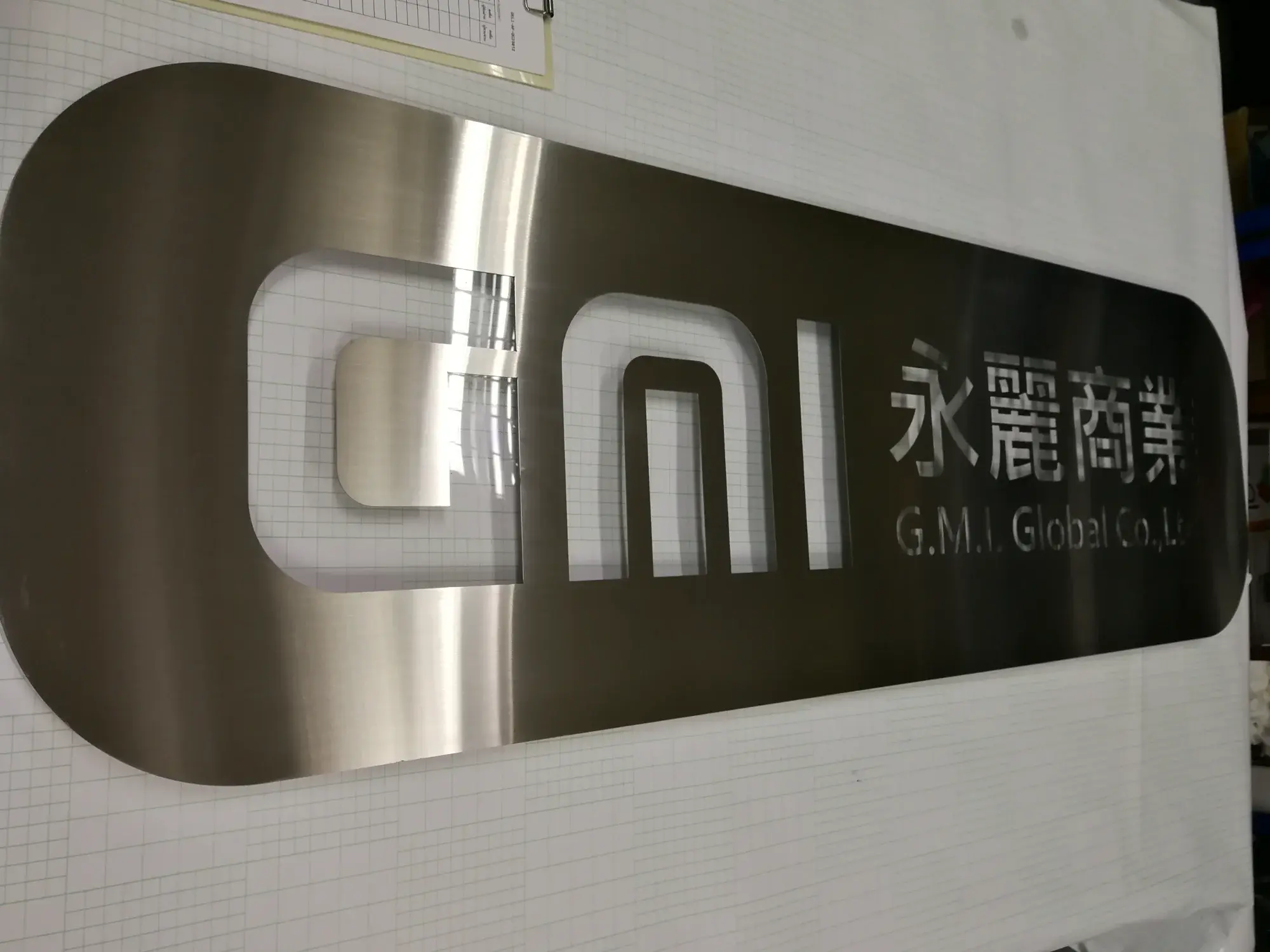 ป้ายสแตนเลสแฮร์ไลน์โลโก้ GMI 永麗商業 G.M.I. Global Co., Ltd บนพื้นดำ
