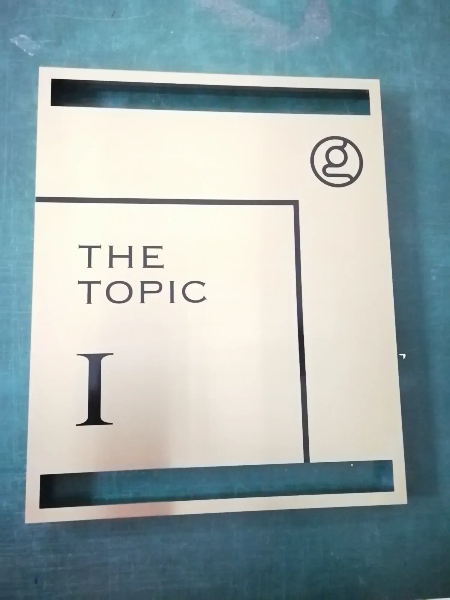 ป้ายชื่อคอนโด The Topic ตัวอักษรสแตนเลสสีดำบนพื้นสีครีม พร้อมหมายเลขชั้น I และโลโก้