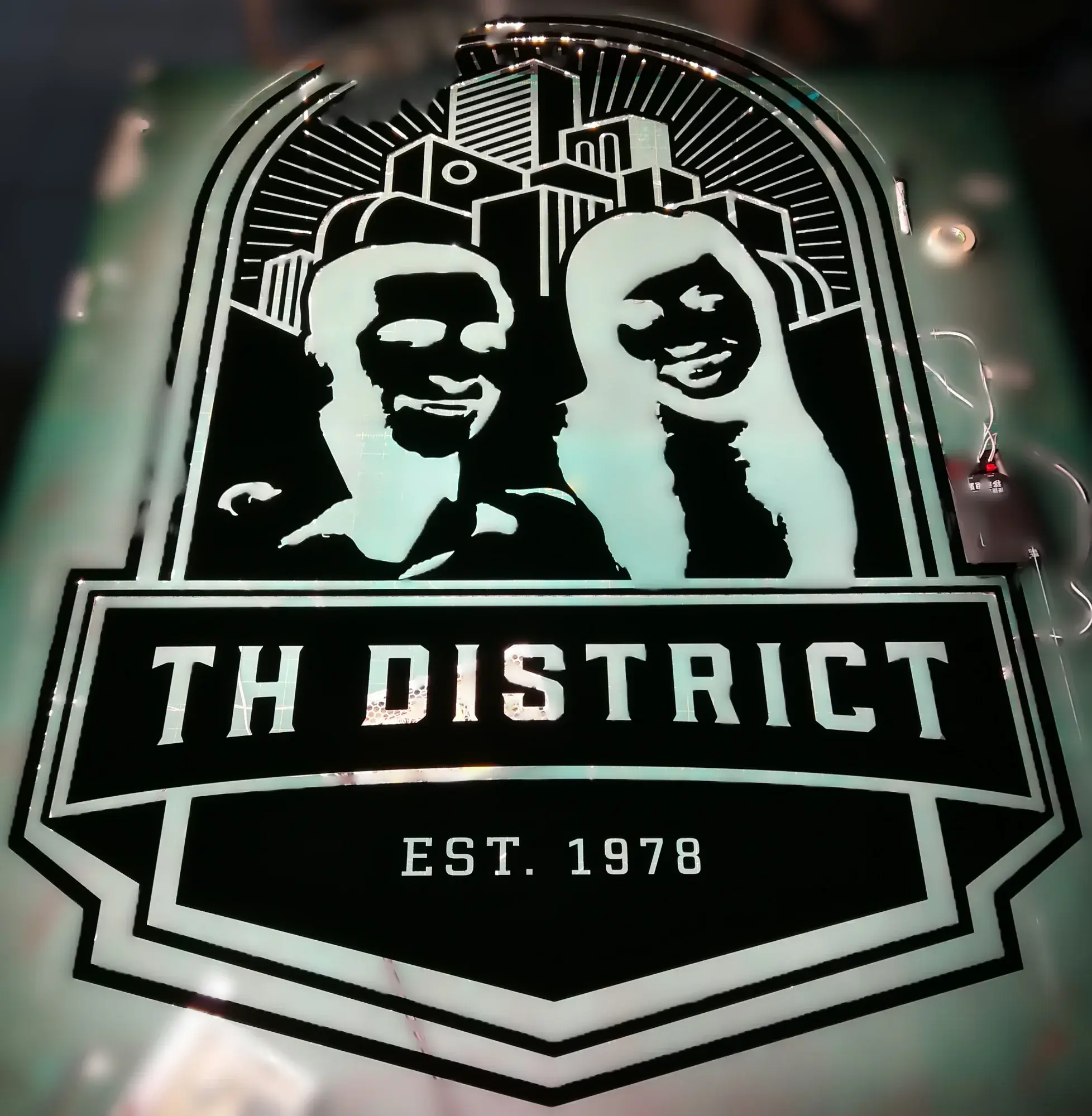 ป้ายสแตนเลสไฟส่องหลัง TH DISTRICT EST. 1978 รูปคู่รักหน้าตึกเมืองสไตล์ Art Deco