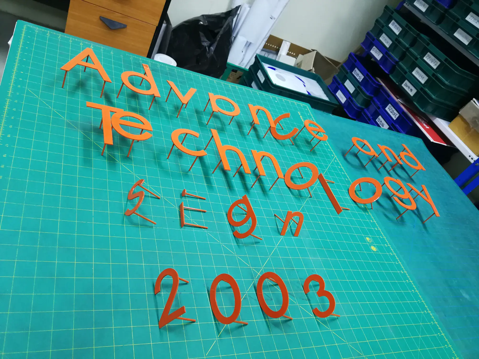 ตัวอักษรอะคริลิกสีส้ม Advance and Technology Sign 2003 บนโต๊ะตัดในโรงงาน