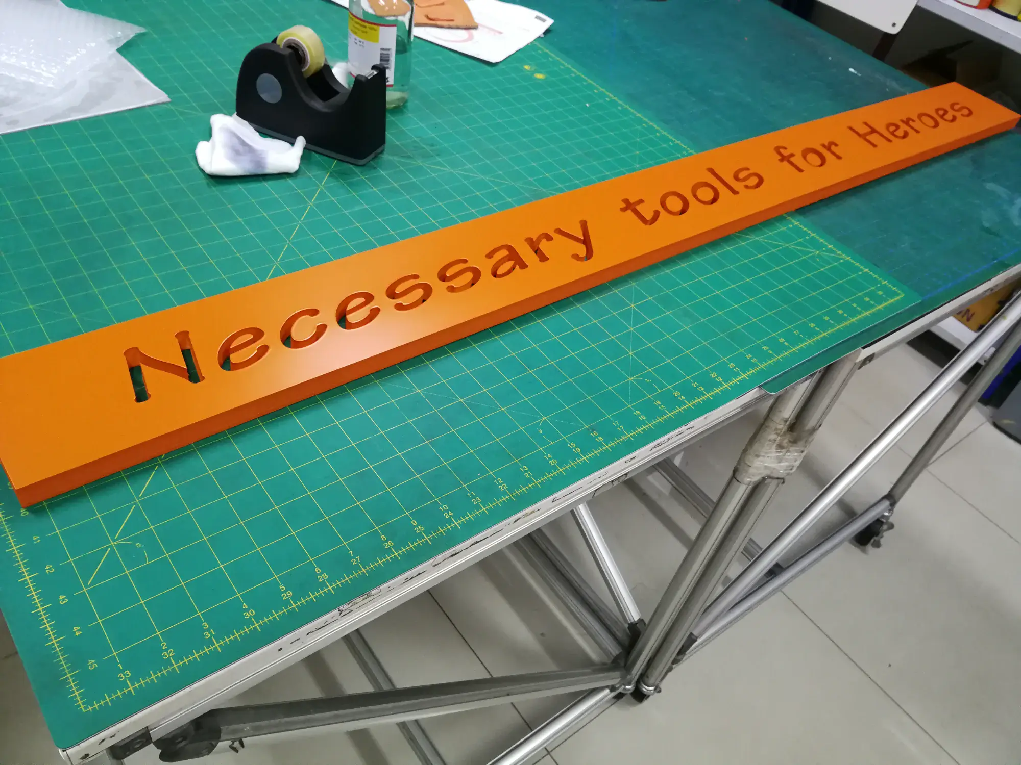 ป้ายอะคริลิกสีส้มตัวอักษรฉลุ Necessary tools for Heroes บนโต๊ะตัด