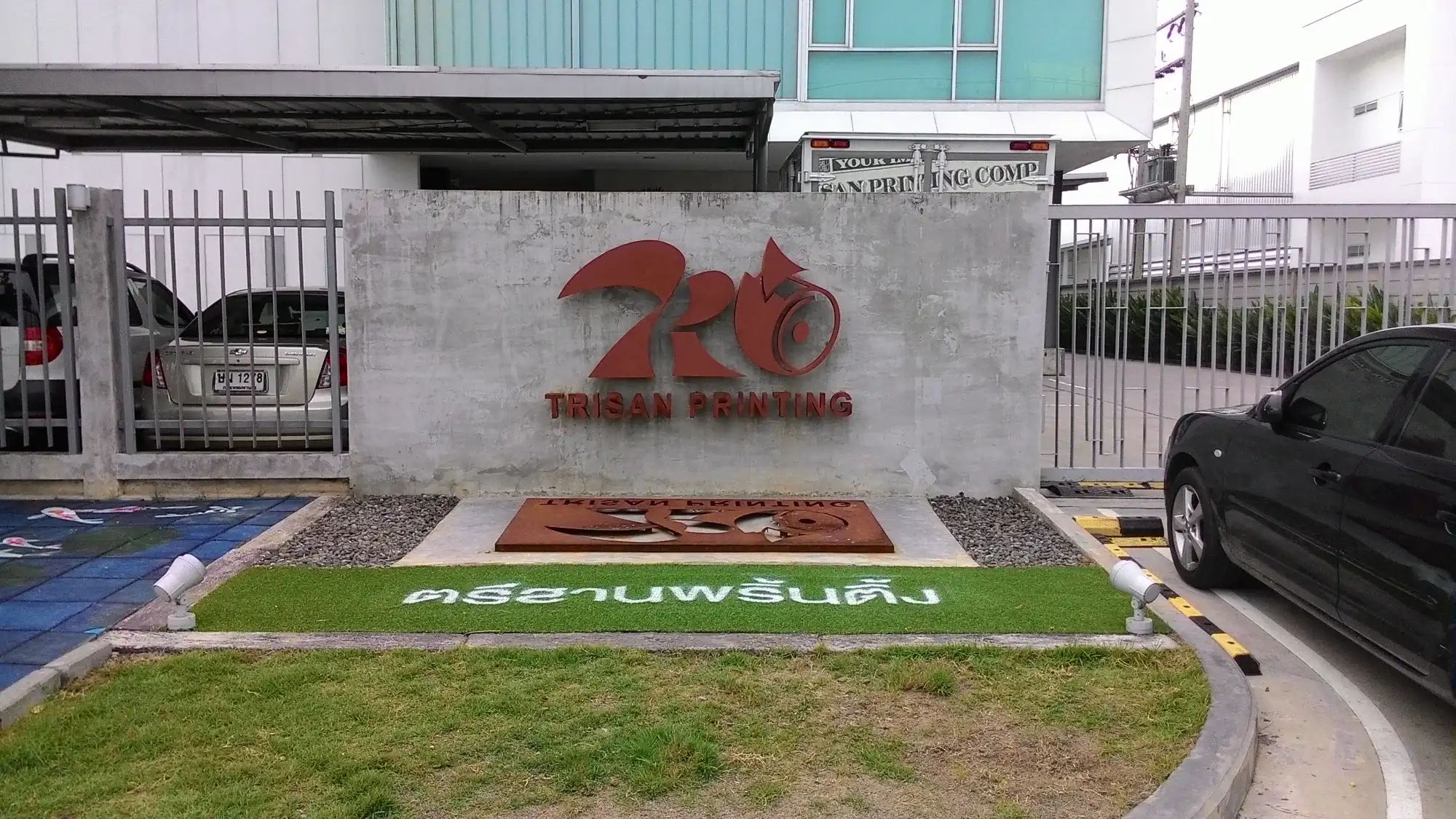 ป้ายสแตนเลสสีแดงโลโก้ TRISAN PRINTING รูปกระรอกติดผนังปูนหน้าอาคารบริษัท