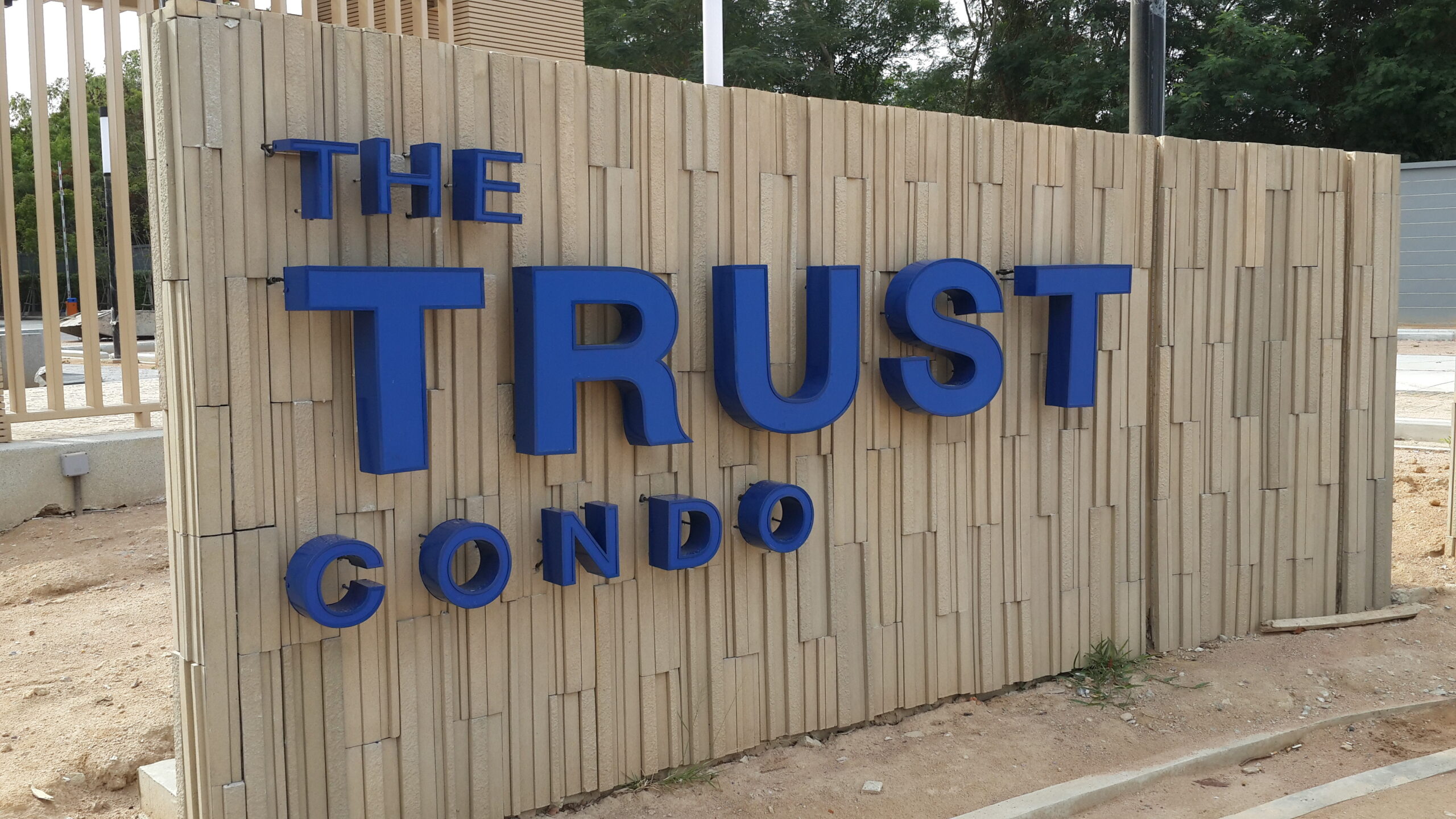 ป้ายคอนโดมิเนียม The Trust Condo ตัวอักษรสีน้ำเงินติดผนังหิน