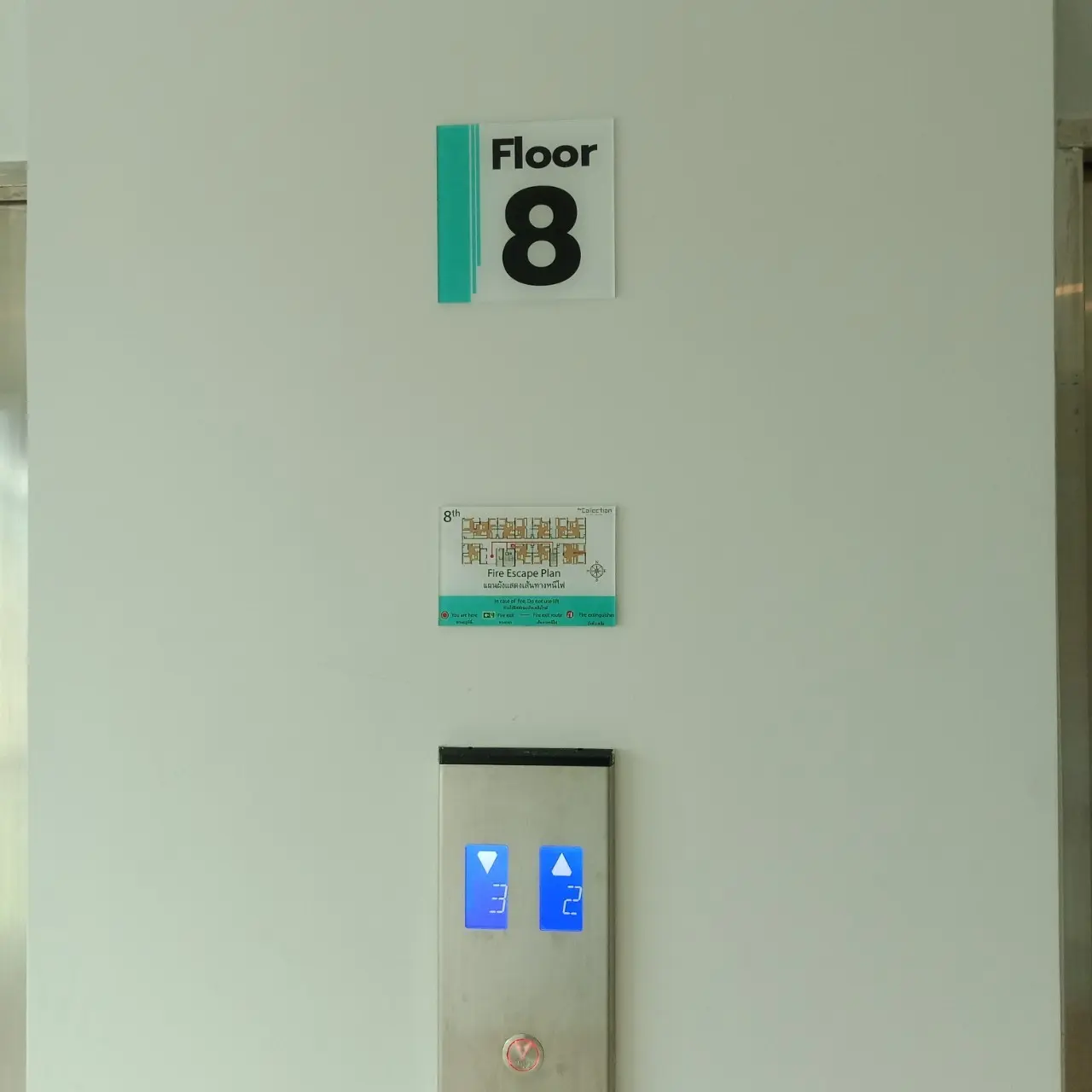 ป้ายบอกชั้น Floor 8 สีขาวเขียว พร้อมป้ายแผนผังหนีไฟ ติดผนังข้างลิฟต์คอนโด