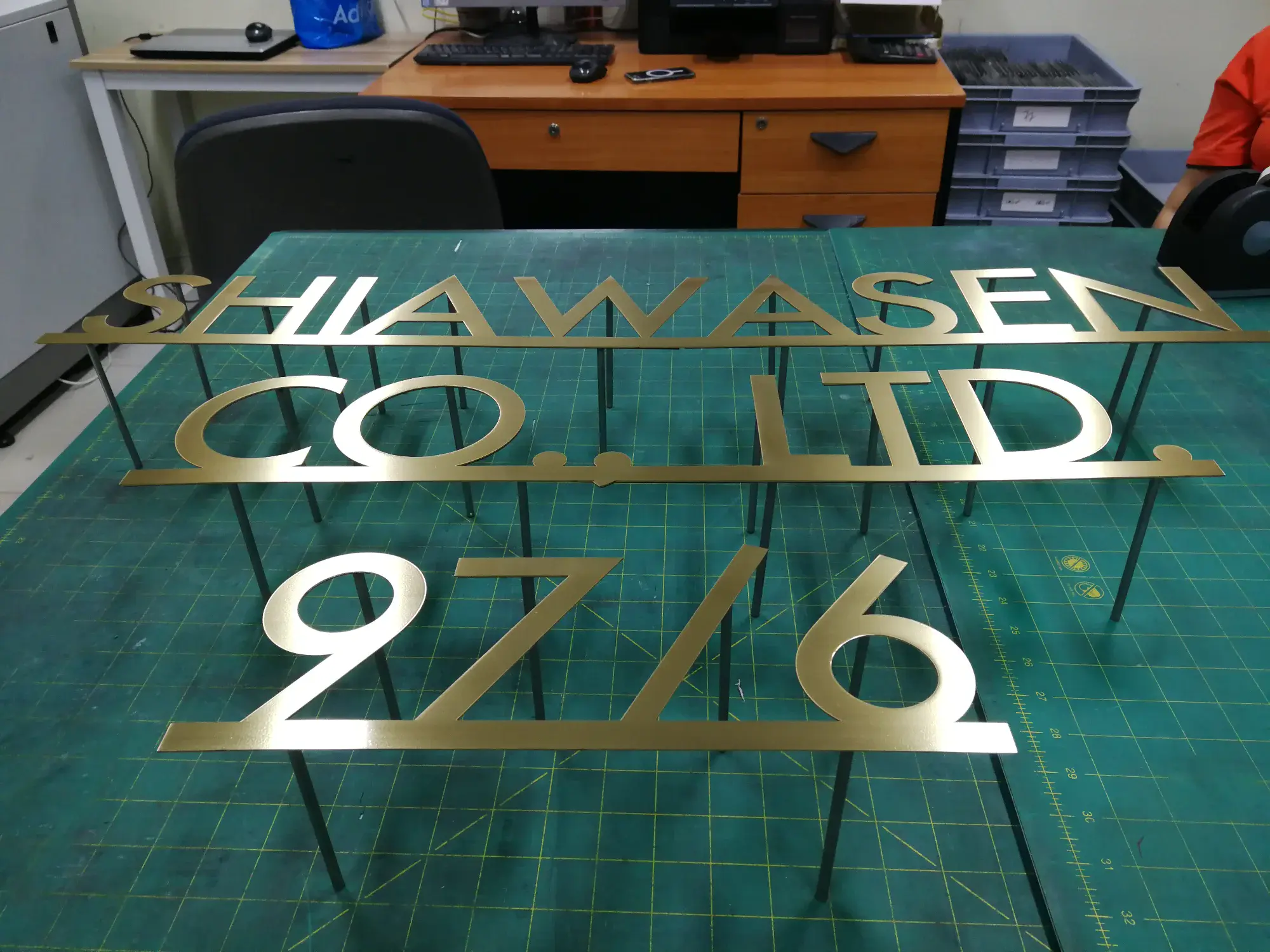 ป้ายทองเหลืองฉลุชื่อบริษัท SHIAWASEN CO., LTD. พร้อมเลข 9716 บนโต๊ะตัด