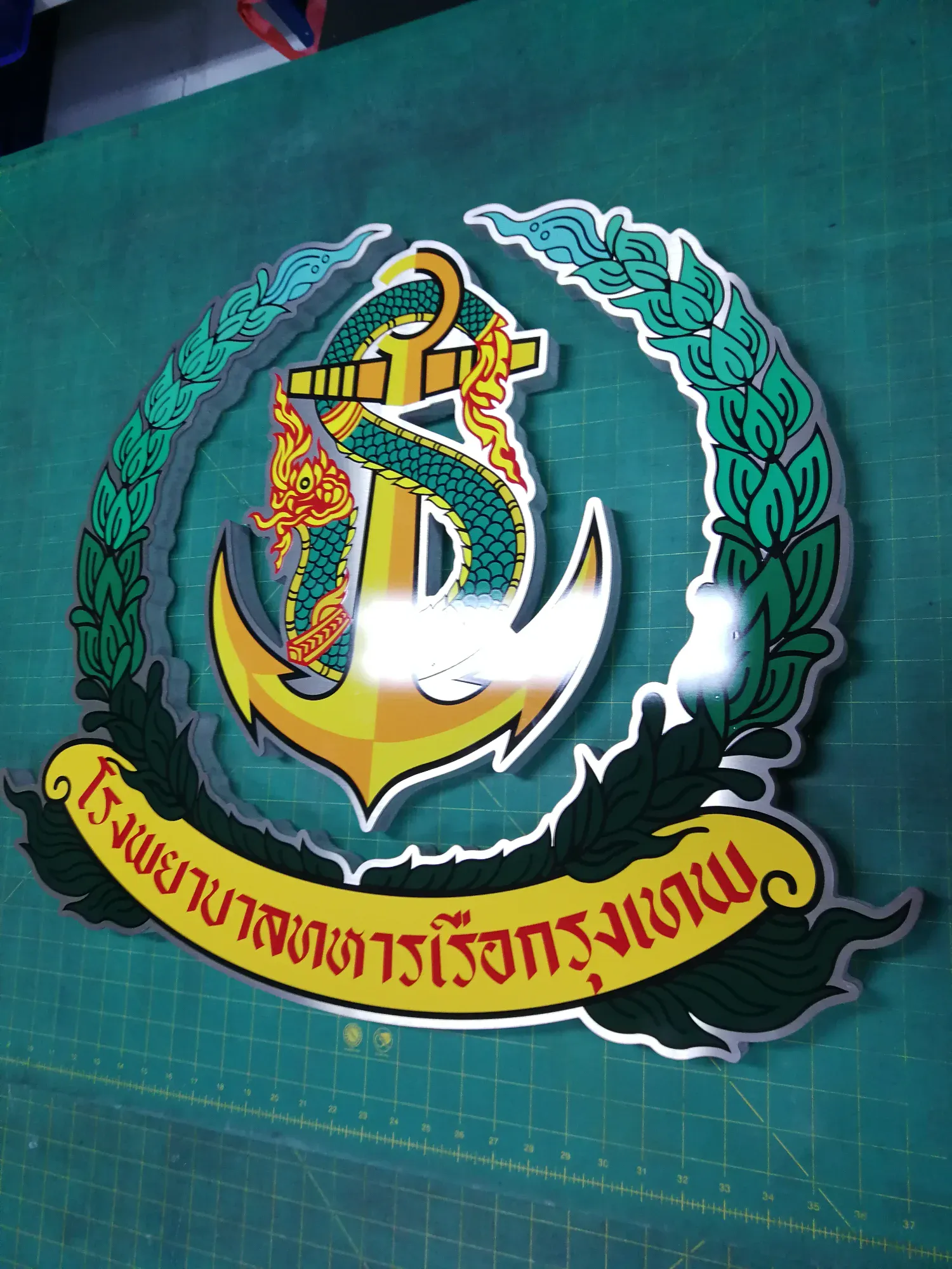 ป้ายตราสัญลักษณ์โรงพยาบาลทหารเรือกรุงเทพ สแตนเลส รูปสมอทองพันด้วยพญานาคสีเขียวล้อมด้วยช่อชัยพฤกษ์