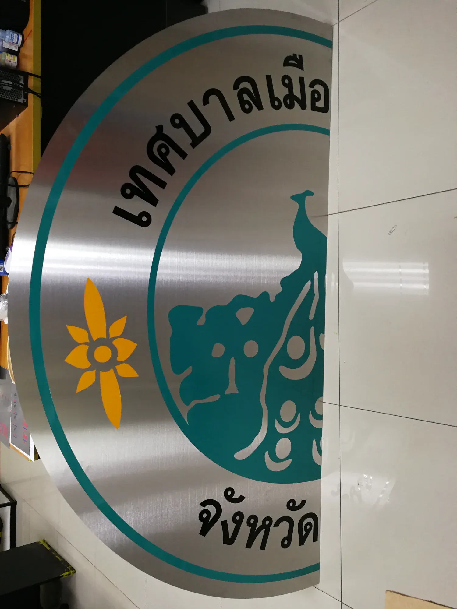ป้ายตราสัญลักษณ์เทศบาลเมือง สแตนเลส รูปนกยูงสีเขียวอมฟ้าพร้อมดอกไม้สีทอง