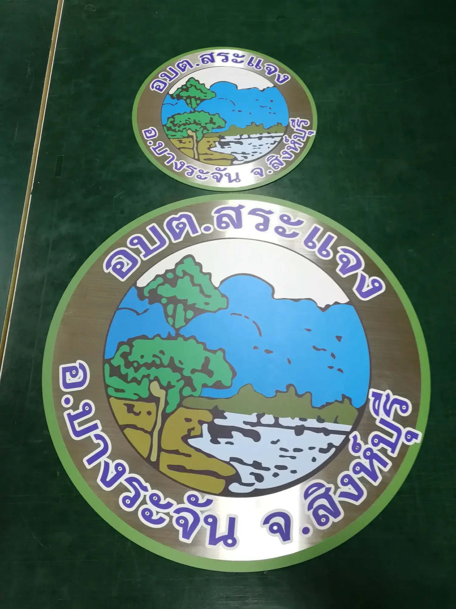 ป้ายตราสัญลักษณ์ อบต.สระแจง อ.บางระจัน จ.สิงห์บุรี สแตนเลส รูปทิวทัศน์ต้นไม้หน้าผาและน้ำตก