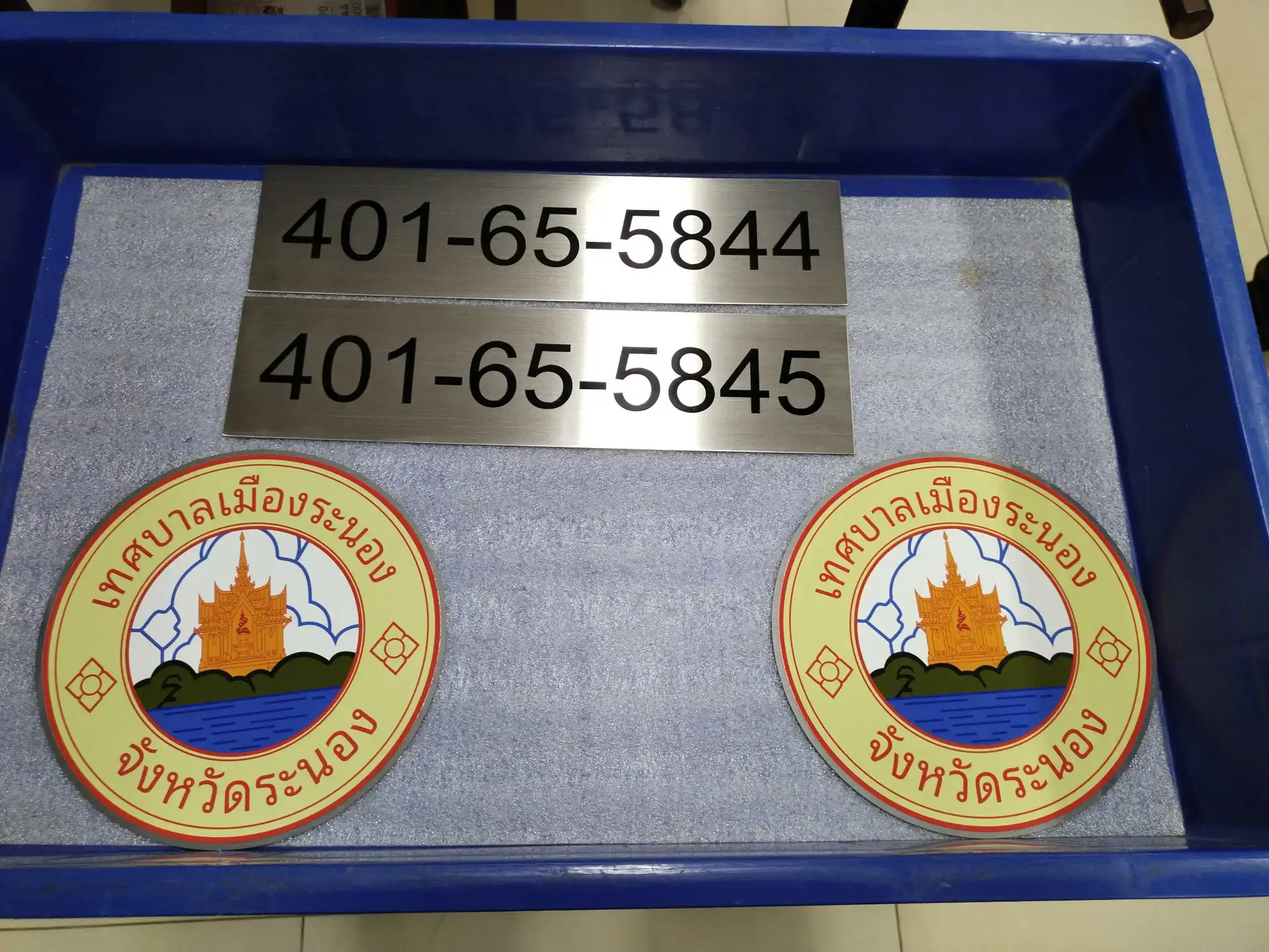 ป้ายตราสัญลักษณ์เทศบาลเมืองระนอง อลูมิเนียมขอบแดงพื้นเหลืองรูปเจดีย์ทองและภูเขาริมทะเล